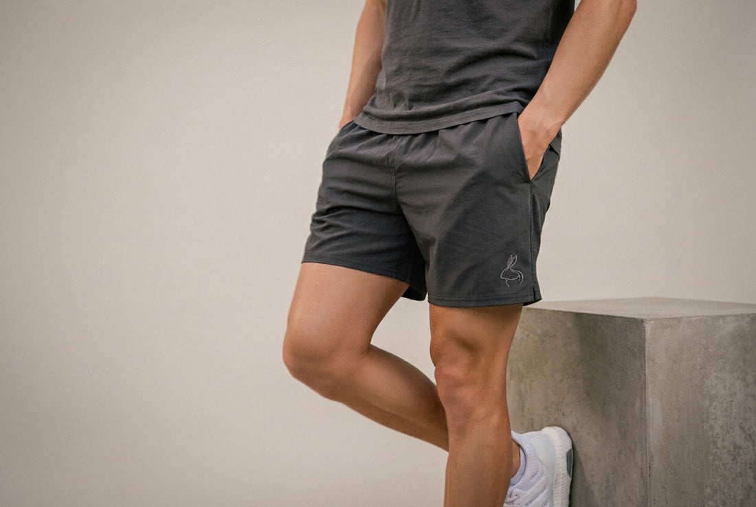 Person wearing dark above-the-knee shorts and a charcoal T-shirt against a neutral wall