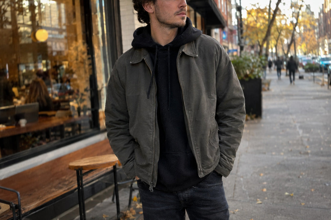 Man in black hoodie layered under olive jacket on an autumn city street — minimalist cold weather outfit, Biliping
