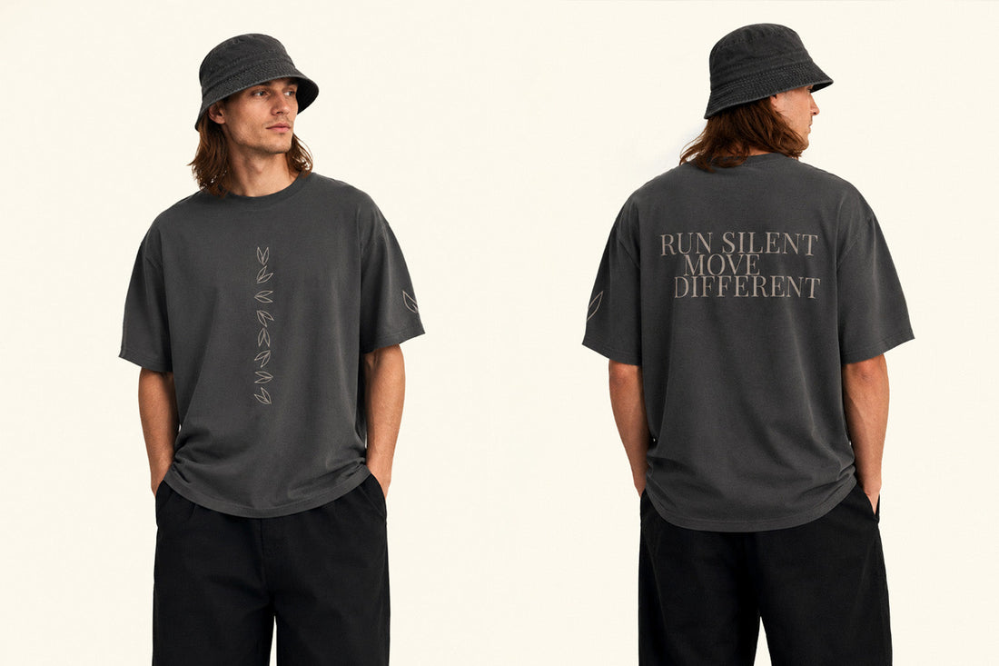 Front and back view of a model wearing a graphite oversized T-shirt, with a vertical leaf graphic on the front and the words “RUN SILENT MOVE DIFFERENT” on the back.