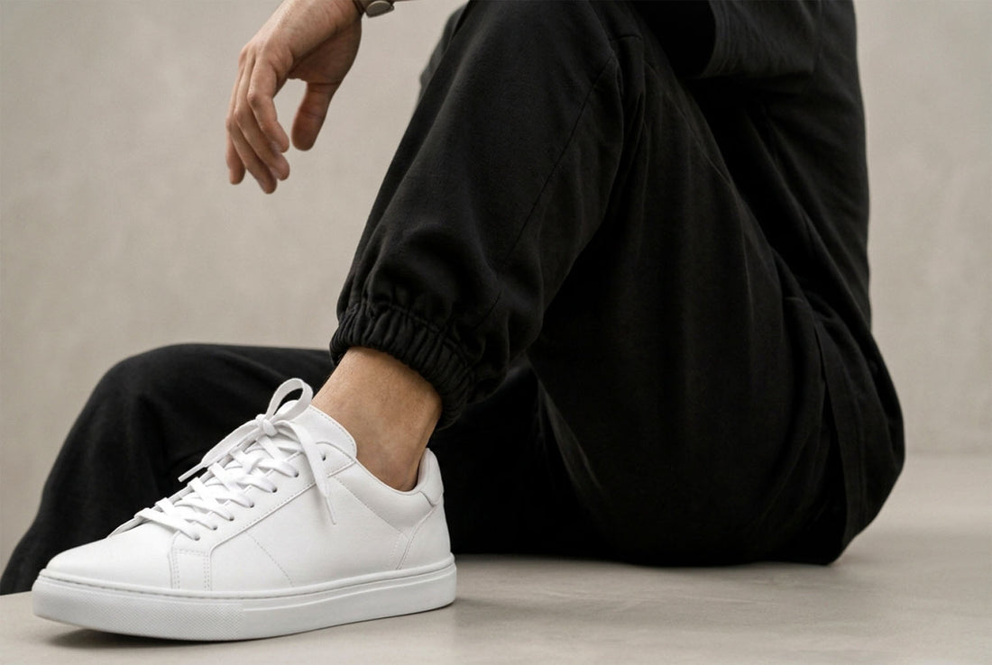 Close-up of white low-top sneakers paired with black cuffed sweatpants and a black T-shirt.